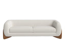 A front view of the Amala sofa, featuring a curved body in cream bouclé fabric that is cradled by a sculptural, solid wood base.