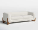 A three-quarter view of the Amala sofa, highlighting the seamless curve of its bouclé-upholstered body and the carved details of its solid wood base.