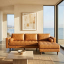 Anita 102-inch tan genuine top-grain leather right-facing sectional sofa with grid-tufted seat cushions, cylindrical bolster pillows, and tapered wooden legs in a sunlit modern living room with ocean views.