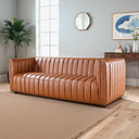 April 86-inch cognac genuine leather sofa with vertical channel tufting displayed in a bright modern living room on light hardwood floors with a beige area rug.