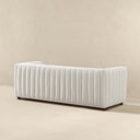Three-quarters rear view of the April 86-inch mid-century modern channel-tufted sofa upholstered in textured beige bouclé fabric set against a plain beige background.
