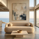 Ava 84 beige boucle sofa with two round sphere pillows in a modern minimalist living room featuring a travertine coffee table and scenic ocean view through large windows.