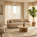 Ava 84 beige boucle sofa in a minimalist, neutral-toned living room with a round travertine coffee table, textured rug, and potted fiddle-leaf fig tree.