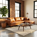 Bayley 107-inch cognac vegan eco-leather right-facing sectional sofa with chaise in a sunlit industrial loft living room with exposed brick walls, cream area rug, and mid-century coffee table.