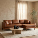 Bayley 107-inch cognac brown vegan eco-leather right-facing sectional sofa styled in a warm organic minimalist living room with a round travertine coffee table and textured cream area rug.