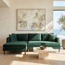 Bayley 107" dark green velvet left-facing sectional sofa with matching throw pillows and tapered wooden legs in a sunlit modern living room with ocean views.