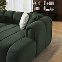  Close-up of a modern dark green French bouclé sectional sofa with channel tufting, rounded armrest, and decorative throw pillows in a stylish living room.