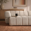 Close-up of the Burntwood 114-inch light brown chenille power slider sofa with vertical channel tufting, featuring a black mug on a book atop the cushion in a modern living room.