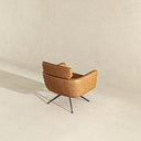 Rear three-quarter view of a modern Camila swivel armchair upholstered in tan genuine leather with tailored stitching details, supported by a sleek black metal four-star base set against a neutral textured background.