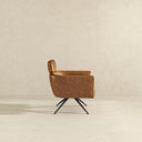 Side profile view of a modern swivel armchair upholstered in tan genuine leather, featuring a cushioned headrest, deep seat with structured track arms, and a four-pronged matte black metal swivel base, set against a neutral, minimalist textured background.