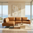 Carla 109-inch tan genuine leather left-facing sectional sofa with tapered wood legs in a sunlit modern living room with ocean views