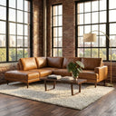 Carla 109-inch tan genuine leather left-facing sectional sofa styled in an industrial loft living room with exposed brick walls, large grid windows, a slatted wooden coffee table, and a plush shag area rug.