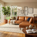 Carla 109-inch tan genuine leather right-facing sectional sofa styled in a sunlit modern living room with a textured area rug, decorative pillows, and potted fiddle-leaf fig tree.