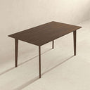 Carma 63-inch rectangular walnut dining table featuring rounded corners, a smooth wood grain top, and slender tapered legs against a neutral background.
