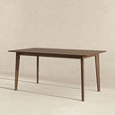 Carma 63-inch rectangular walnut dining table featuring a smooth wooden tabletop and four slim tapered legs, set against a neutral textured background.
