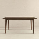 Modern rectangular walnut dining table with a beveled tabletop and tapered legs, set against a neutral beige textured backdrop.
