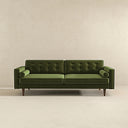 Casey mid-century modern olive-green velvet upholstered sofa featuring a button-tufted back, matching cylindrical bolster pillows, and tapered dark wood legs on a beige background.