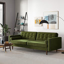 Casey tufted back olive-green velvet upholstered sofa with cylindrical bolster pillows and tapered wood legs, styled in a bright modern living room with wall art and an arched floor lamp.