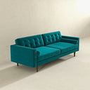 Three-quarters of the Casey mid-century modern teal velvet upholstered sofa featuring a button-tufted back, matching cylindrical bolster pillows, and tapered dark wood legs on a beige background.