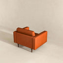 Rear three-quarter view of the Casey burnt orange velvet armchair featuring sleek track arms, a plush back cushion, and tapered dark wood legs against a neutral backdrop.