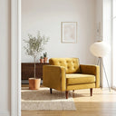 Mid-century modern Casey gold velvet armchair with button-tufted back and tapered wooden legs in a sunlit living room on a woven rug.