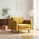 Casey gold velvet armchair with button-tufted back and tapered wooden legs in a sunlit mid-century modern living room