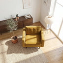 Casey gold velvet armchair with tufted back cushion on a textured woven rug in a sunlit living room beside an indoor olive tree and paper lantern floor lamp.
