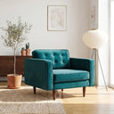 Casey teal velvet armchair with button-tufted back and tapered wooden legs in a sunlit modern living room setting.