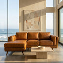 Chase 91-inch tan genuine leather left-facing sectional sofa with tapered wooden legs in a sunlit modern living room with floor-to-ceiling ocean view windows and a beige travertine coffee table.