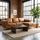 Chase 91-inch tan genuine leather right-facing sectional sofa with chaise lounge in an industrial loft living room featuring exposed brick walls, large black-framed grid windows, a dark wood coffee table, and a potted fiddle-leaf fig plant.