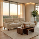 Chiara 97-inch cream genuine leather sectional sofa with chaise in a modern living room with floor-to-ceiling windows overlooking a sunset landscape, dark wood coffee table, and textured area rug.