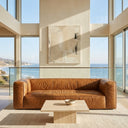 Chloe 92-inch tan genuine leather sofa in a modern minimalist living room with a travertine coffee table, neutral abstract wall art, and panoramic ocean views through floor-to-ceiling windows.