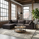 Concetta 121-inch dark gray fabric modular sectional sofa with chaise styled in a modern industrial loft living room with exposed brick walls, large black-framed windows, a round two-tier wood coffee table, and an arched floor lamp.