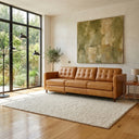 Cora 94-inch tan leather electric reclining left-facing sofa with button-tufted back cushions, styled in a modern living room on a textured cream rug with large abstract wall art.