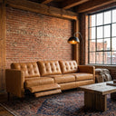 Cora 94 tan leather electric reclining left-facing sofa with the recliner extended, set in an industrial loft living room with an exposed brick wall, an arc floor lamp, and a rustic wooden coffee table.