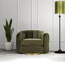 An olive green velvet swivel armchair featuring vertical channel tufting and a round brass base, styled on a light carpet against a paneled wall with a potted snake plant on the left and a tall floor lamp with a green shade on the right.