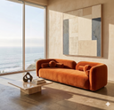 Modern living room with an orange sofa, abstract mirror, and ocean view.