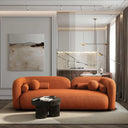 Elissa 93-inch Japandi burnt orange boucle sofa featuring a curved, low-profile design and matching spherical pillows in a minimalist living room. The modern rust-colored couch is set on a cream shag rug next to a dark wood coffee table, bathed in natural light from large glass window.
