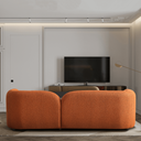 Rear view of the Elissa 93-inch Japandi burnt orange boucle sofa featuring a curved, low-profile design in a minimalist living room. The modern rust-colored couch is set on a cream shag rug facing a flat screen tv, bathed in natural light from large black-framed glass doors.