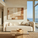 Elissa 93-inch Japandi ivory boucle sofa with a curved design and matching round and bolster throw pillows in a minimalist living room. In the foreground, a travertine coffee table sits on a woven jute rug. The background features a large neutral abstract painting on the wall and a floor-to-ceiling window with a scenic ocean view.