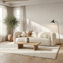Elissa 93-inch Japandi ivory boucle curved sofa with matching pillows in a bright minimalist living room, featuring a light wood coffee table, textured cream rug, large potted olive tree, and a black arched floor lamp.