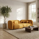Modern Japandi living room featuring the Elissa 93 curved mustard yellow boucle sofa, styled with round matching throw pillows, a dark wood coffee table, a potted olive tree, and a textured area rug under warm natural sunlight.