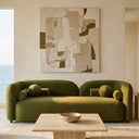 Elissa 93 Japandi olive green velvet sofa with a curved backrest and round cushions, positioned in a minimalist living room featuring a travertine coffee table, abstract art, and ocean views.