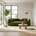 A bright Japandi-style living room featuring the Elissa 93-inch olive green velvet sofa, a round wooden coffee table, a tall potted fiddle-leaf fig plant by a large black-framed window, and a modern black arched floor lamp on a cream shag rug.