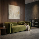 Japandi-style Elissa 93-inch olive green velvet sofa with rounded arms and bolster pillows, styled with a beige throw blanket. The minimalist living room features a vertical wood slat accent wall, abstract wall art, concrete floors, and a black bookshelf against a textured concrete wall.