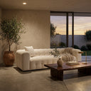 Modern Elizia 86-inch cream boucle Chesterfield sofa with deep tufting in a contemporary living room, featuring a live-edge wood coffee table, potted olive tree, and sunset view through large glass doors.