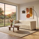 Enno 91-inch mid-century modern cream velvet sofa with vertical channel tufting in a contemporary living room, featured with a round wooden coffee table, textured rug, arched black floor lamp, and abstract wall art.