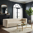 Enno 91-inch Mid-Century Modern cream velvet sofa with vertical channel tufting in a moody living room featuring dark gray paneled walls, a gold glass coffee table, and a fiddle-leaf fig plant.