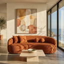 Enzo 89-inch Japandi curved sofa in burnt orange boucle fabric, styled with matching throw pillows in a modern minimalist living room featuring a travertine coffee table, large abstract painting, and scenic ocean views.