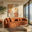 Modern Enzo 89 Japandi curved sofa in burnt orange bouclé upholstery, styled in a minimalist living room with a travertine coffee table, potted olive tree, abstract wall art, and floor-to-ceiling windows overlooking a coastal ocean view.